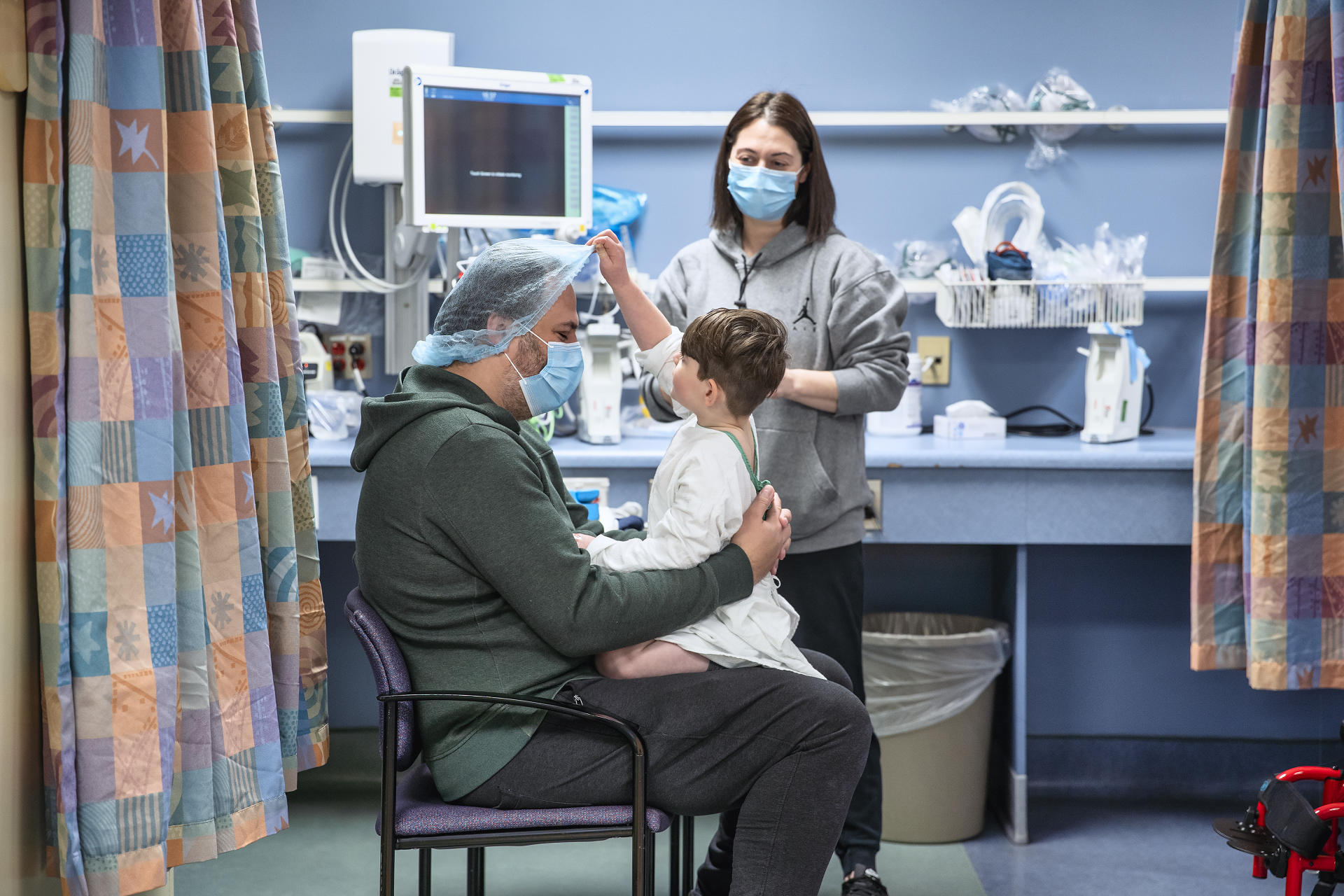Young child sits on adult's lap. Adult is wearing a hair net. Another adult stands behind them.
