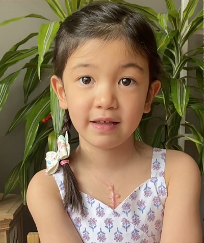 Child sits in front of a plant.