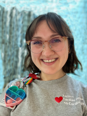 Registered Nurse Larissa Rinkoff smiles wearing a grey SickKids shirt that reads: Larissa, Cardiac Nurse, 4D Cardiology.