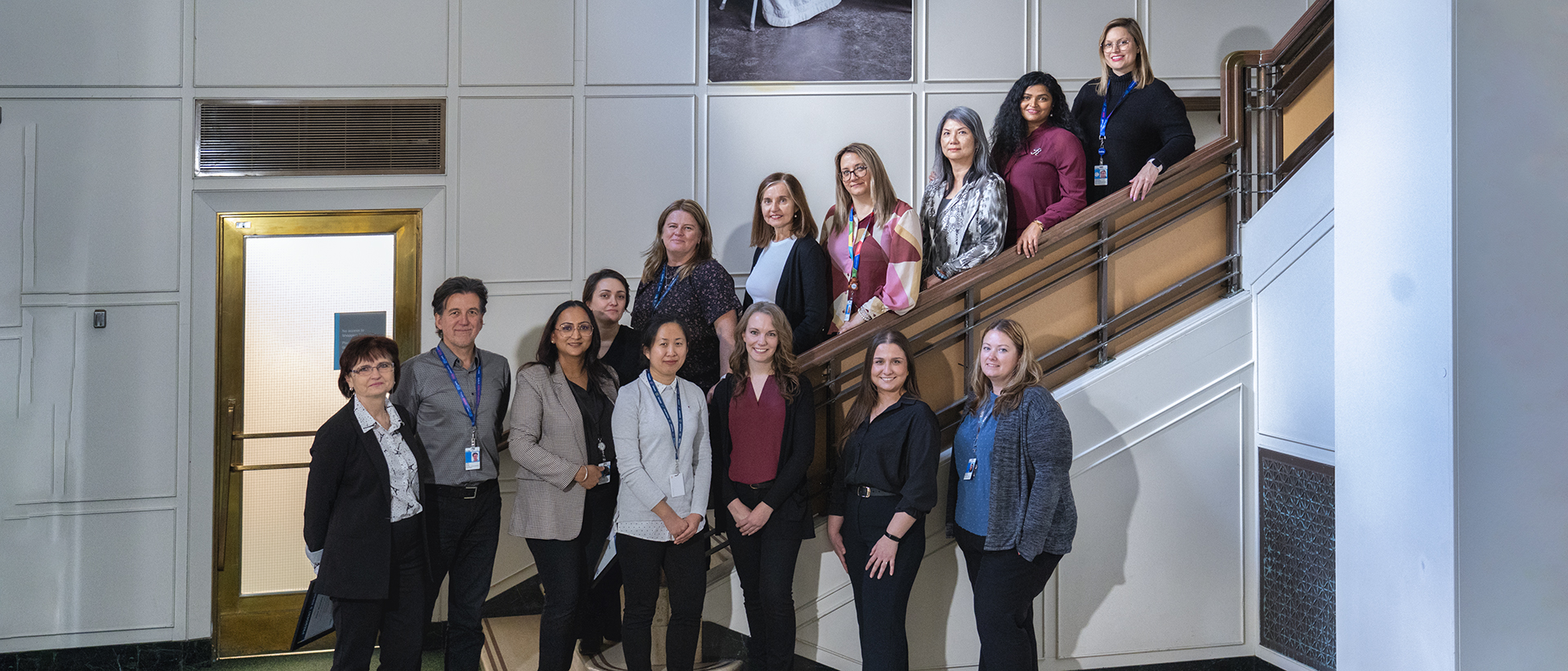 A group of 14 individuals standing together for a photo. Some are standing the steps of a staircase.