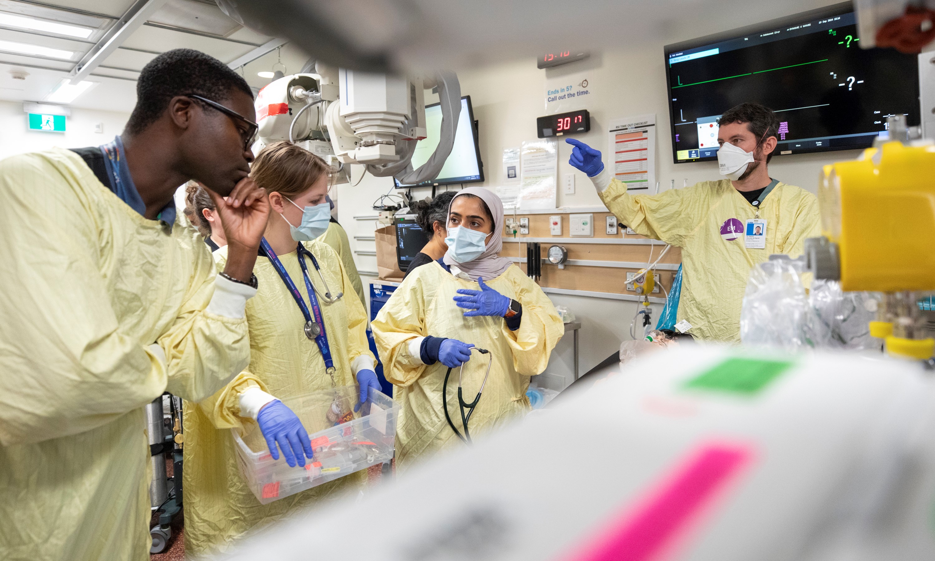 A care team conversing with each other, assesses their simulated patient in the trauma room.  