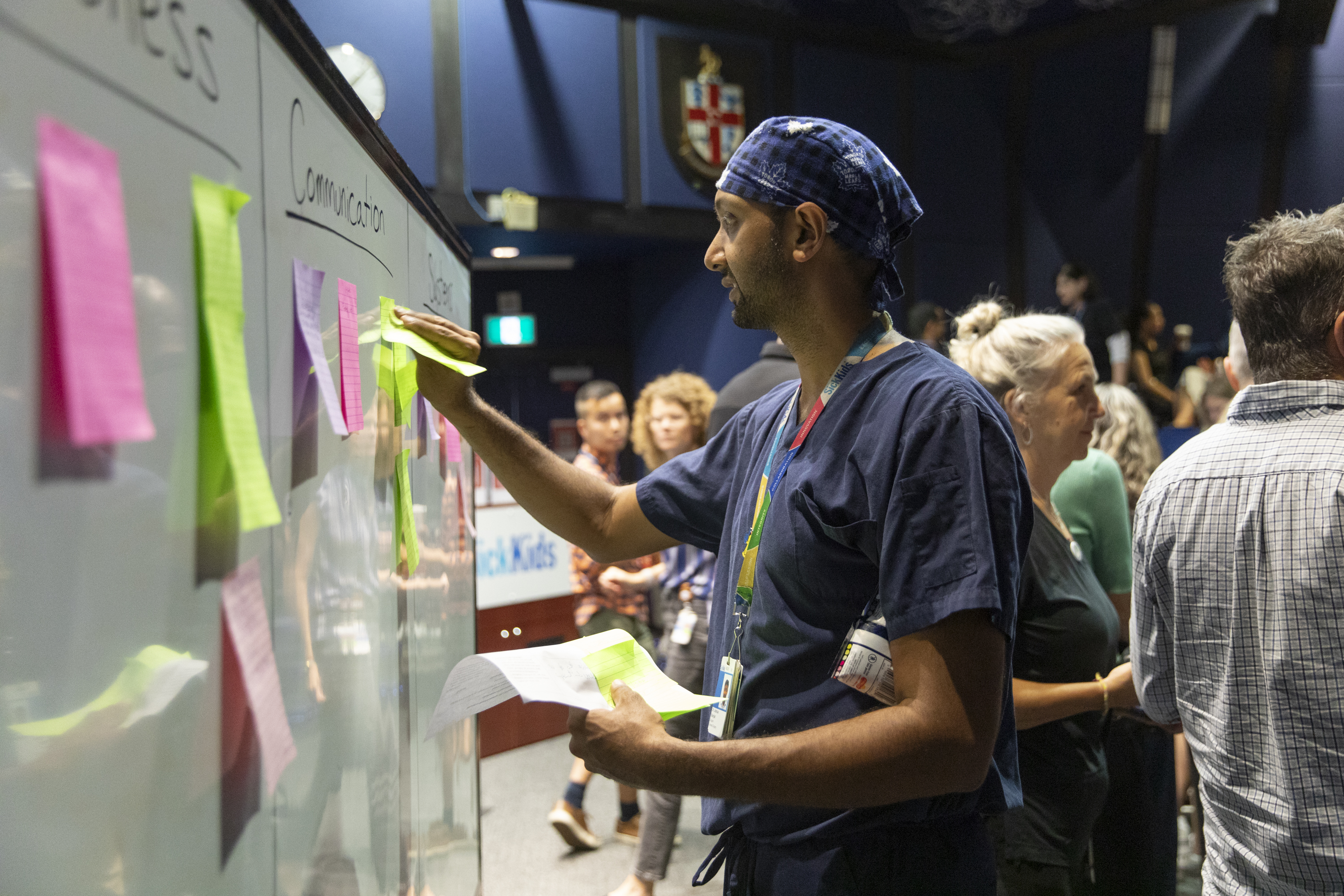 Dr. Joshua Ramjist reviews notes made by staff regarding areas for discussion during the Code Orange simulation debrief session in front of a white board full of sticky notes. 