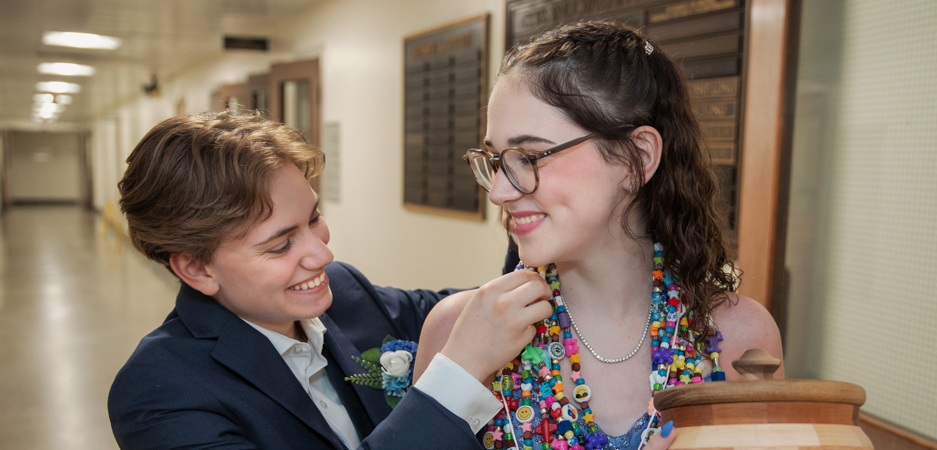 Rylan, dressed in a suit with a corsage, adjusting the bravery beads on Hope's neck.
