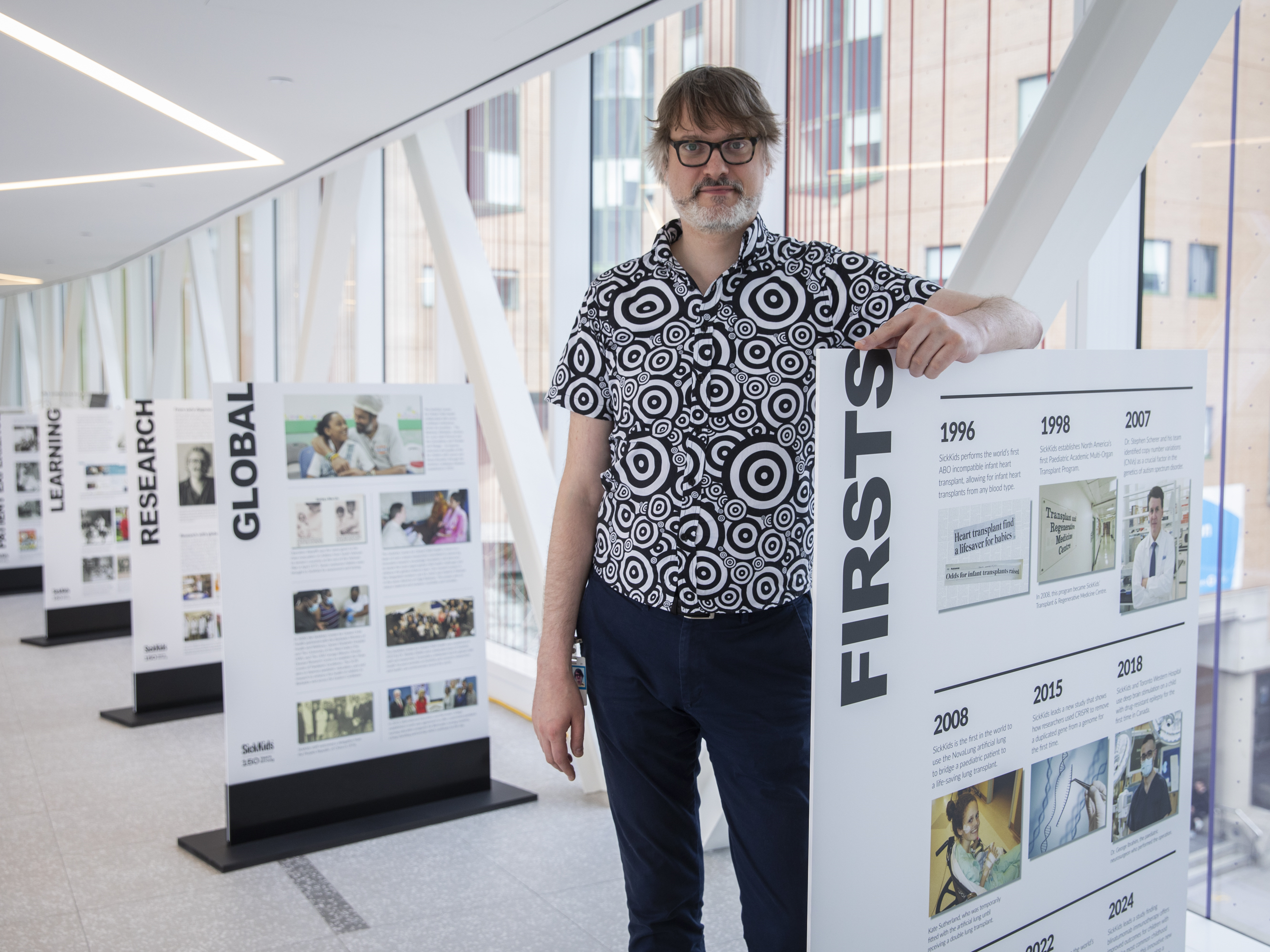 Man in patterned black and white shirt standing next to timeline display showing historical events.