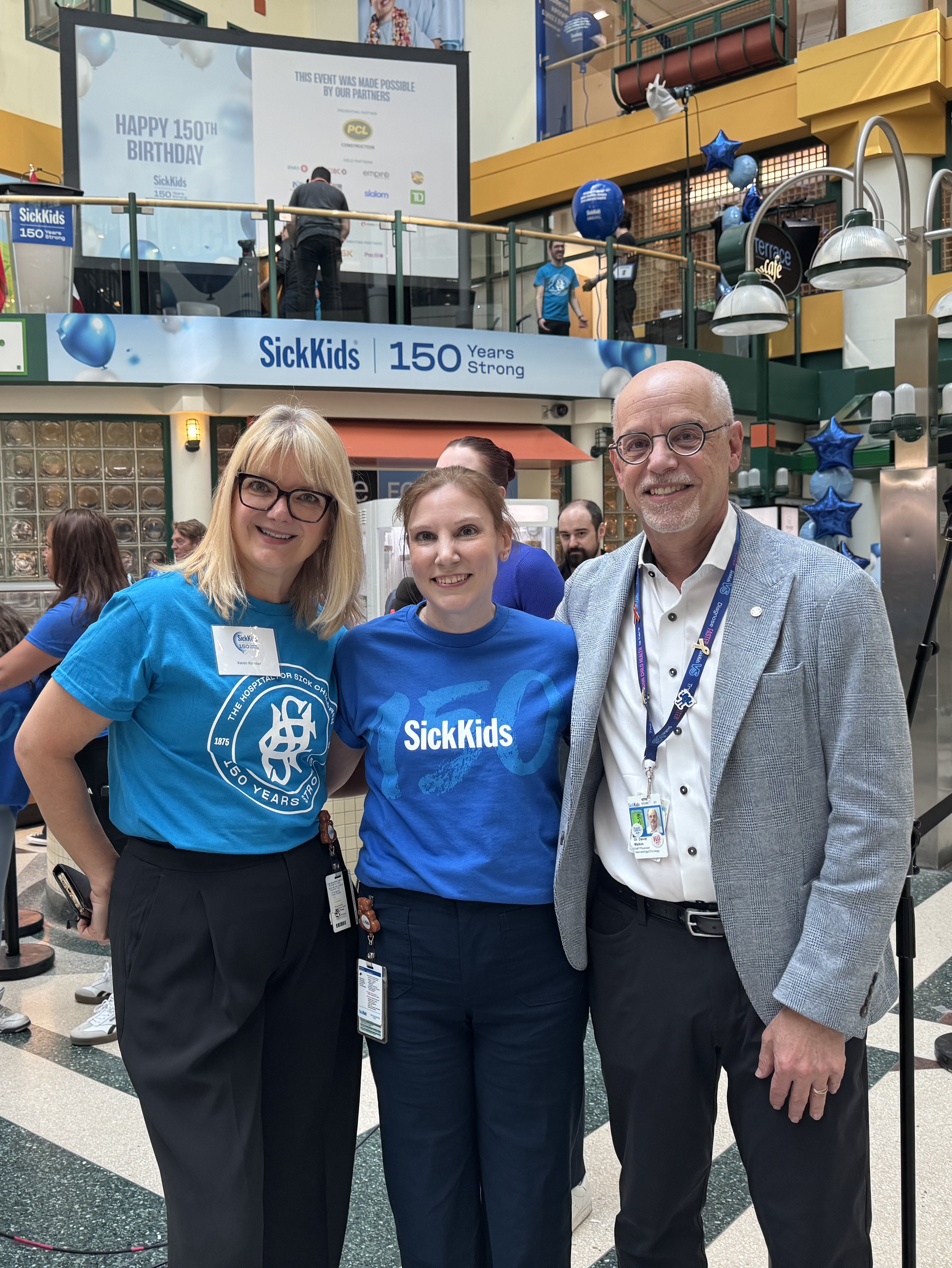 Karen Kinnear, Natalie Wilson and Dr. David Malkin stand in the Atrium at the SickKids 150th birthday celebration. 