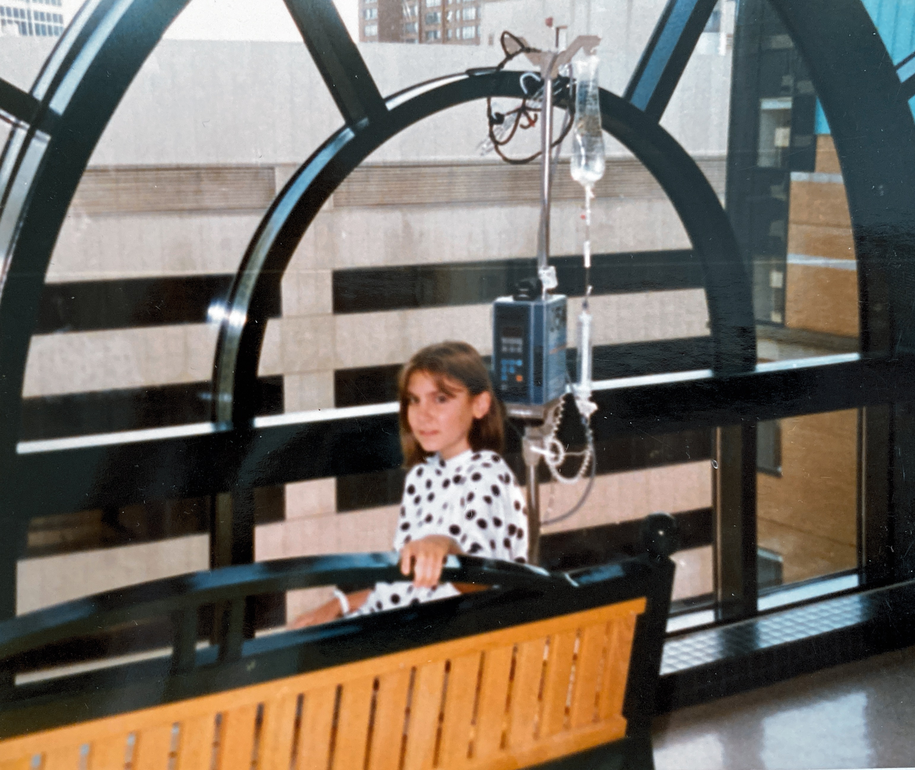 Natalie, age 11, sitting on a bench, facing the camera, with an IV pole behind her.