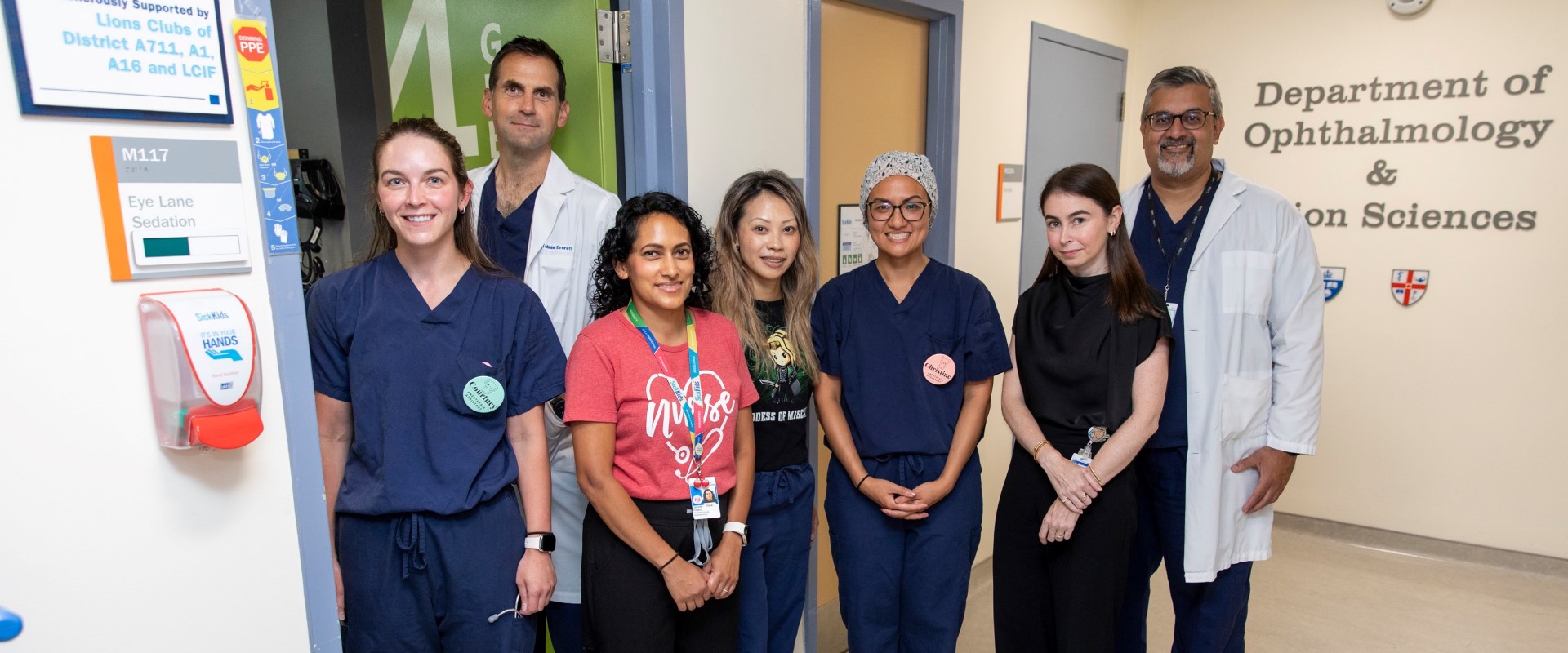 A team of healthcare staff standing in a hospital hallway near a sign for the Department of Ophthalmology and Vision Sciences.