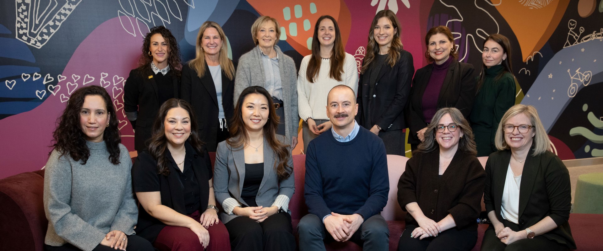 A group of people posed together in front of a colorful mural with abstract shapes and patterns.