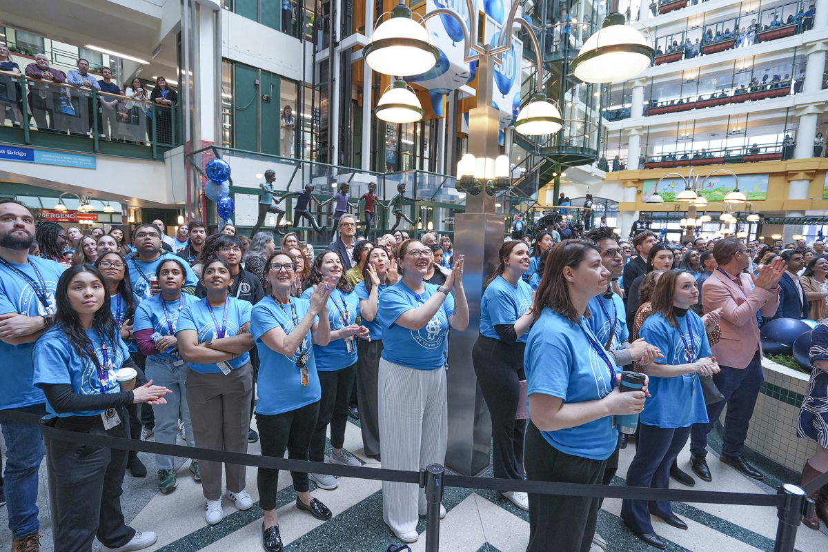 A crowd of people dressed in blue commemorative SickKids 150 t-shirts applauding in the Atrium.