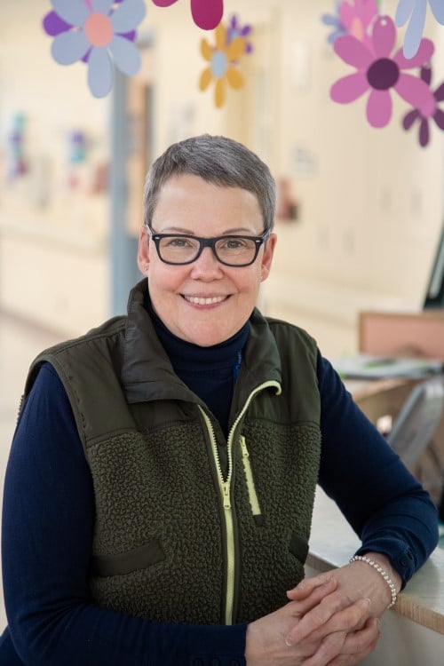 Jane Darch stands smiling in front of a clinic desk with flower decorations hanging above her head.