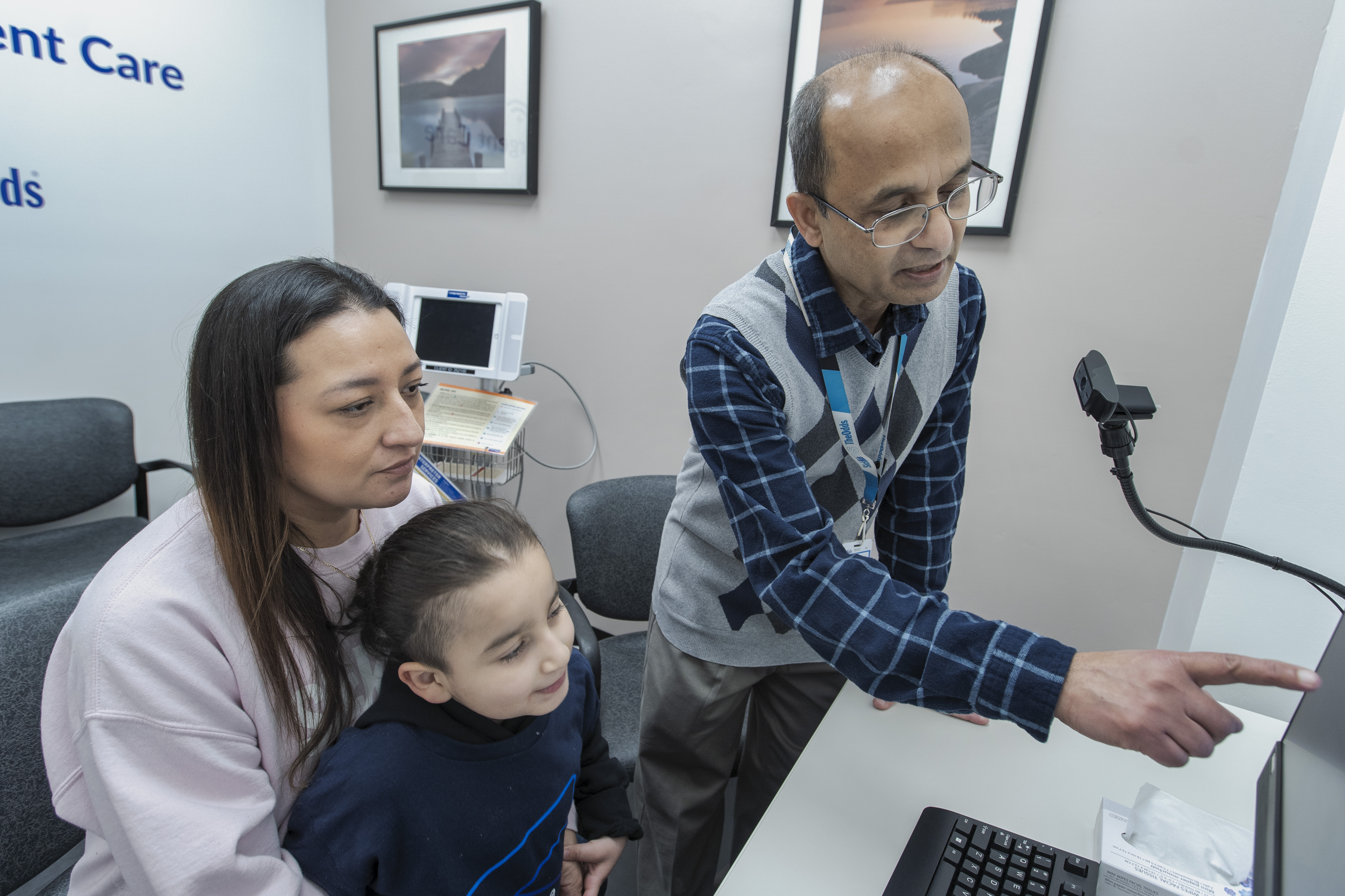 A parent and child seated in front of a computer while a staff member points to something displayed on the screen