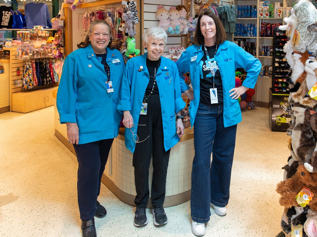 Three women in blue jackets stand inside a vibrant shop.