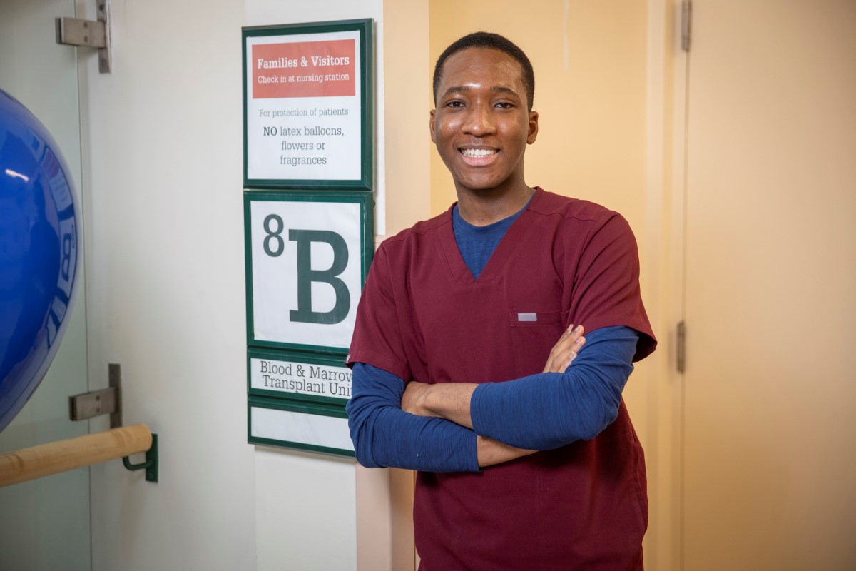 James, wearing burgundy scrubs, stands in front of a sign for unit 8B. 