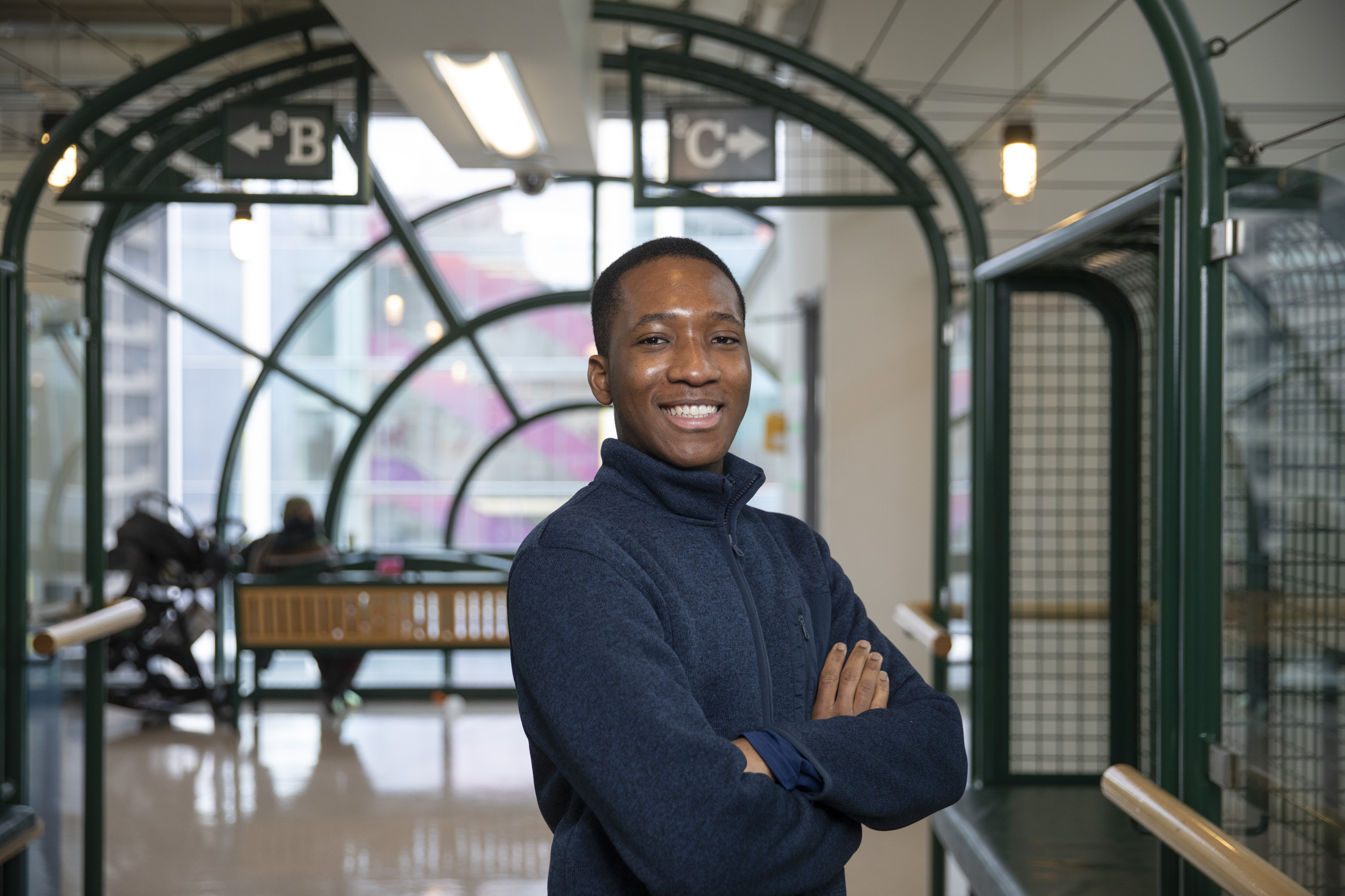 James, wearing a navy blue sweater, stands in the hallway with signs for units 8B and 8C behind him.